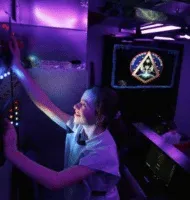 A student at the controls of the original spaceship inside the abandoned church, lit purple.