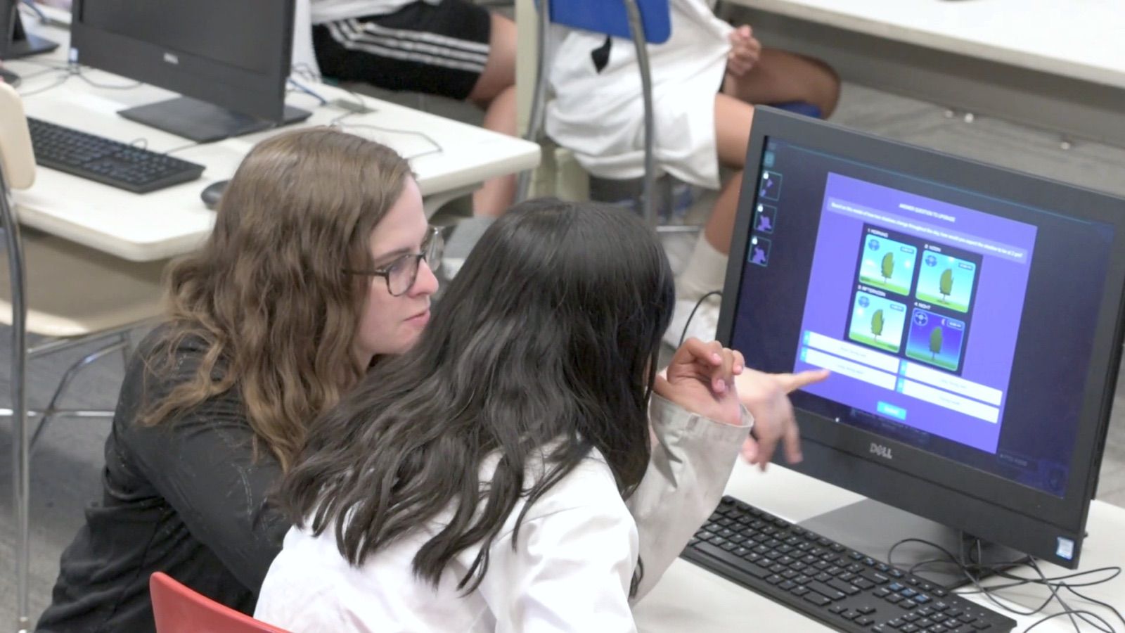A student points to the screen as a teacher leans in beside them, mid-Mission.