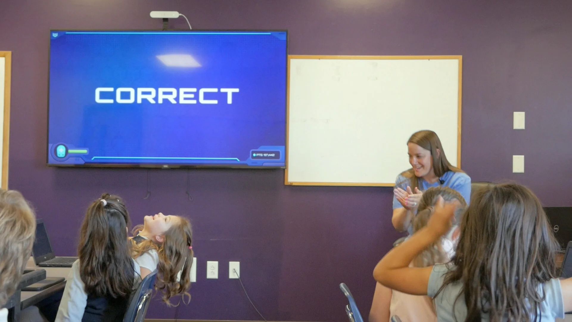 CORRECT shows on the wall screen as students react, one girl tipping her head back laughing.