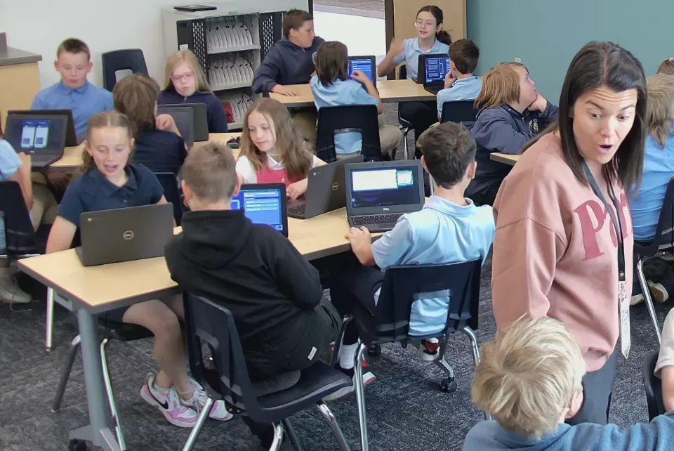 A teacher reacts in surprise as her class works at their laptops.