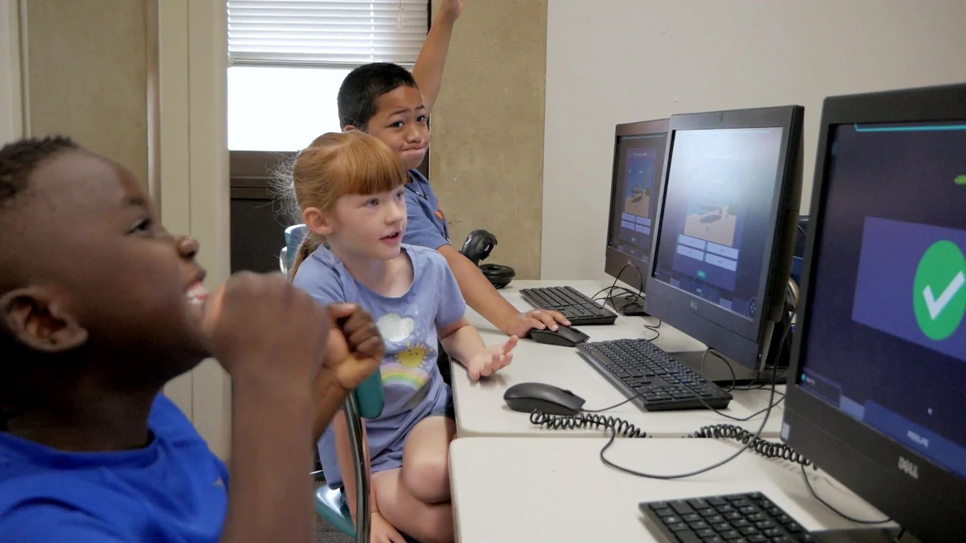A young student beams with a fist at his chin as a green check mark appears on the screen beside him.