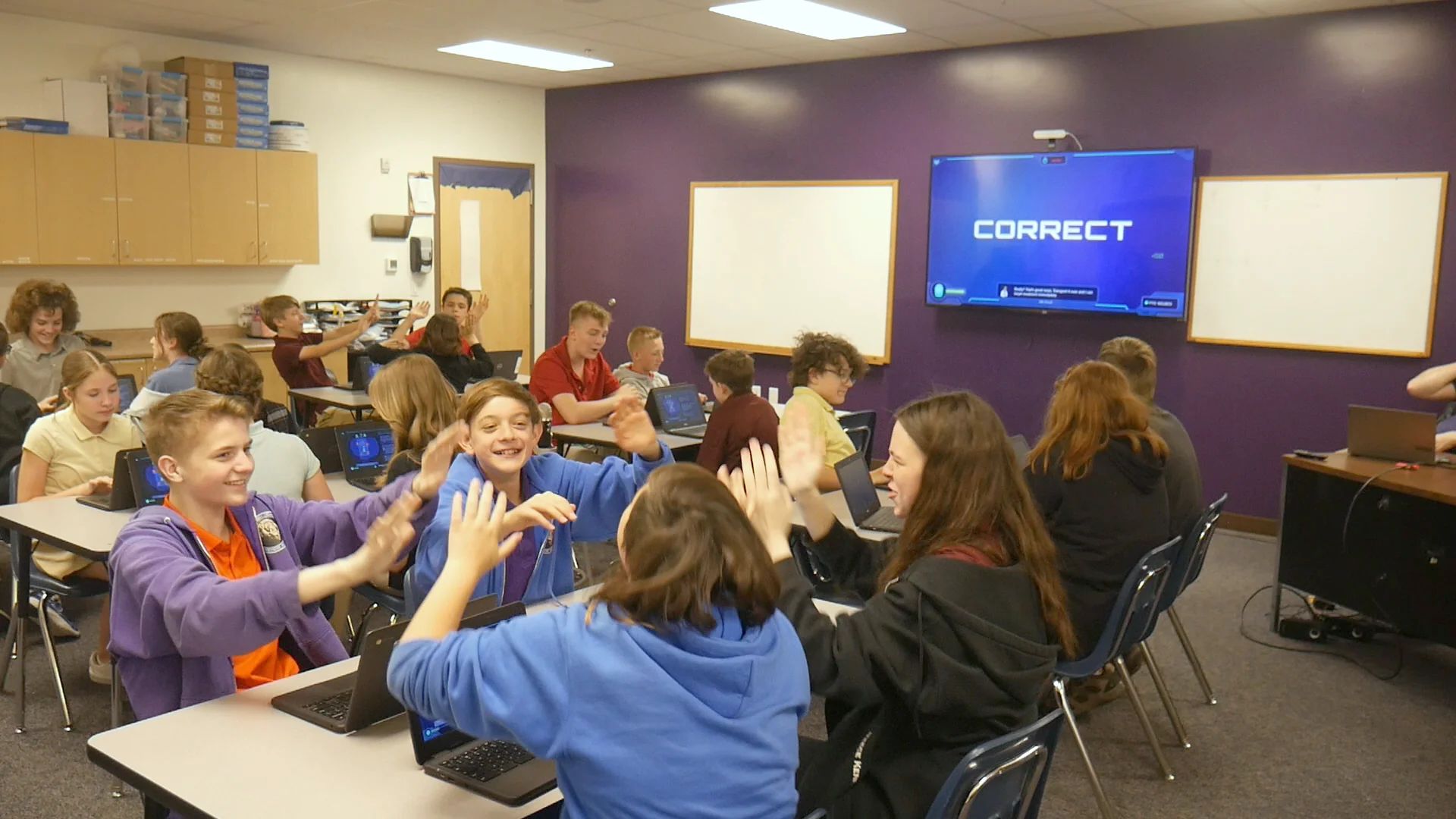 Students high-five across their desks as CORRECT lights up the classroom TV mid-Mission.