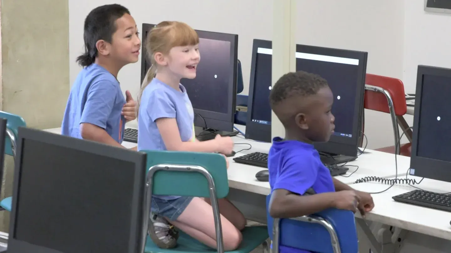 Students in a computer lab grin, one with a thumbs-up, during a Mission.