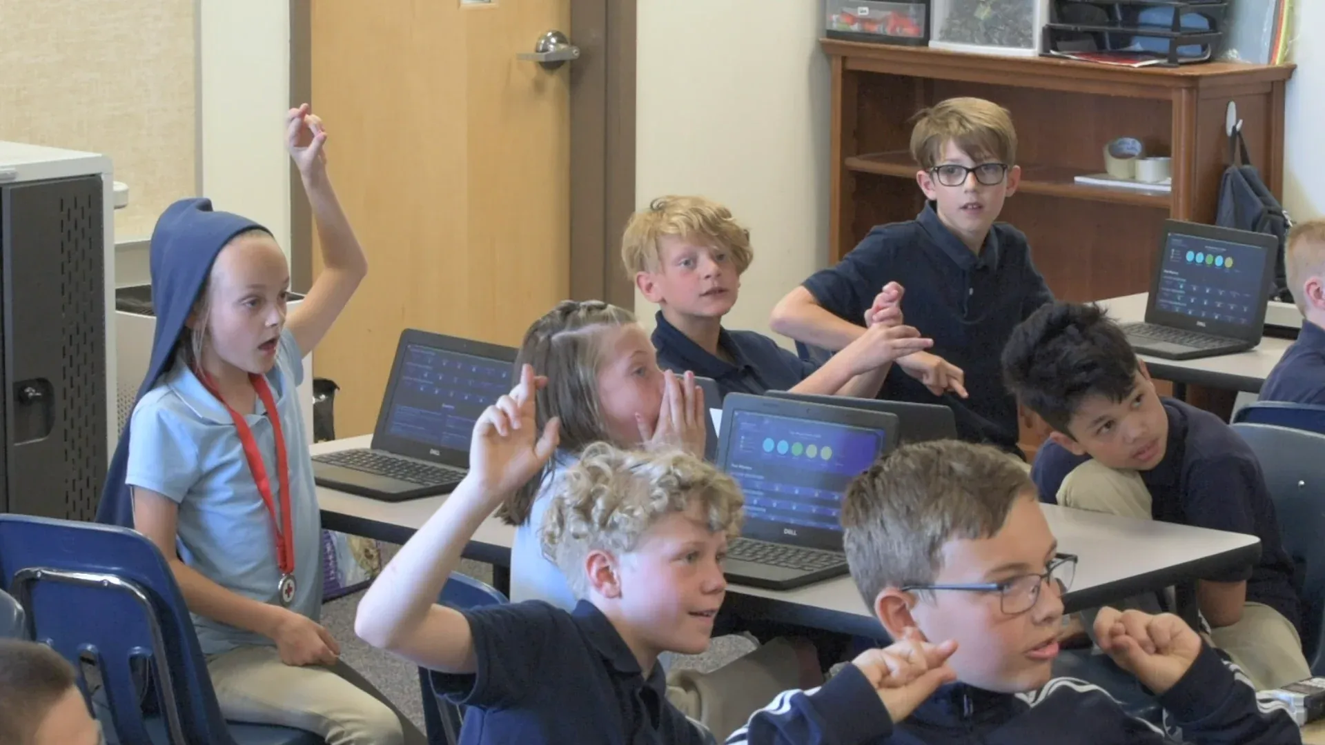 Students raise their hands and gasp in suspense, a girl covering her mouth.