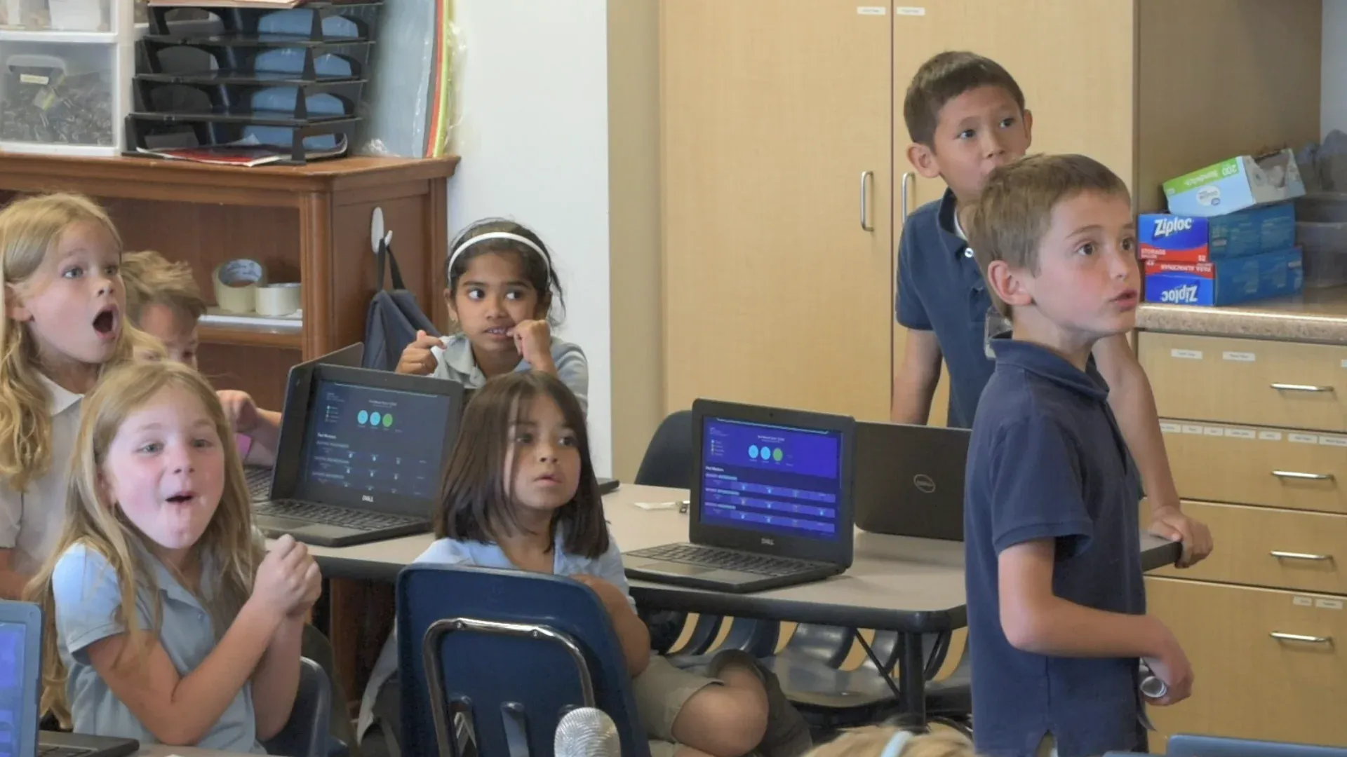 Students crowded around their laptops in the middle of a Mission, some seated, some standing to see.